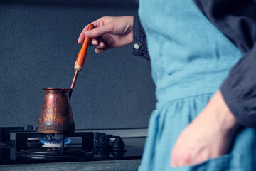 Atmospheric process of making coffee in an old copper cezve, a blurry female figure in a beautiful emerald linen apron. Selective focus