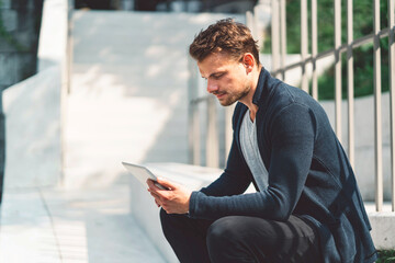 Caucasian man working on the tablet during his lunch break, sitting outside in the sun