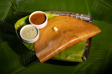 A masala dosa served with sauces and topped with a cube of butter.