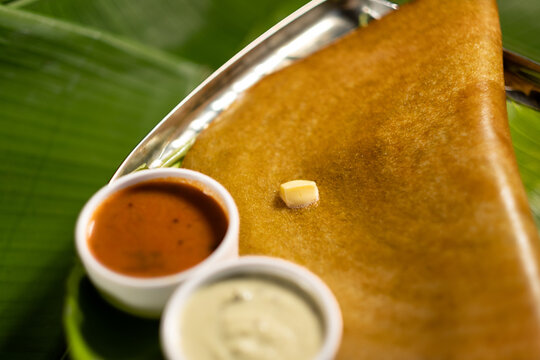 A masala dosa served with sauces and topped with a cube of butter.
