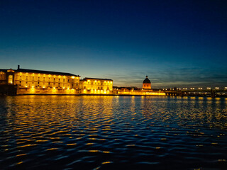 a panoramic view of the garonne river passing through saint pierre bridge with  la grave hospital in the background at night. Toulouse. Light reflection on the garonne river