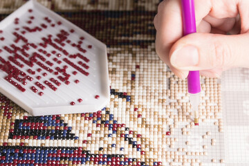 home hobby to draw a picture of rhinestones, multicolored diamond mosaic. the process of gluing a pencil of rhinestones on the canvas of the picture.
