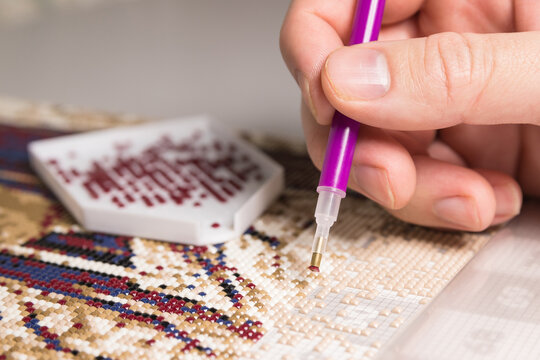A woman collects a diamond mosaic.The process of creating a picture of multicolored rhinestones