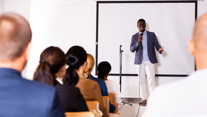 Positive African American with microphone speaking at corporate business event in conference room