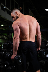 Fototapeta na wymiar A man with a muscular back does an exercise with dumbbells in the gym