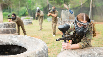 Fototapeta premium Portrait of girl paintball player in mask who is aiming in opponents on paintball field