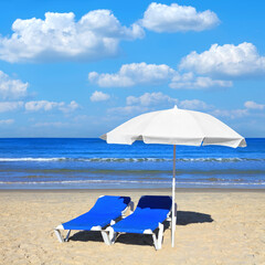 Sandy beach with white sun umbrella and two blue lounges. Magical comfortable warm and clear season of Mediterranean