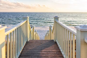 High angle framing view of wooden yellow green white pavilion boardwalk railing stairs steps leading to beach at Gulf of Mexico in Seaside, Florida panhandle sunset and nobody - Powered by Adobe