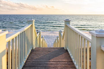 Fototapeta premium High angle framing view of wooden yellow green white pavilion boardwalk railing stairs steps leading to beach at Gulf of Mexico in Seaside, Florida panhandle sunset and nobody