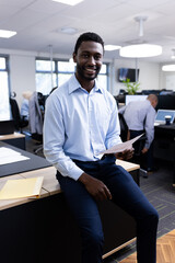 Vertical image of happy african american businessman looking at camera in office