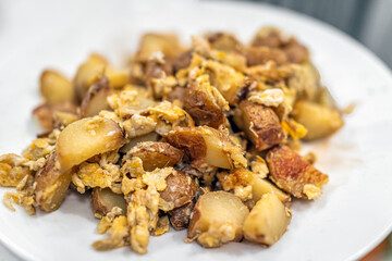 Macro closeup of breakfast or brunch cubed potatoes fried hash on white plate with texture of yellow scrambled eggs