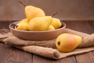 Fresh yellow pears in a bowl on burlap on a stone beige table.