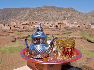 Tea pot with glasses on colorful tray, Ourika valley and High Atlas Mountains in the background....