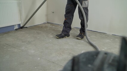 Man in denim pants. Performs cleaning of production facilities. Apartment after renovation with a vacuum cleaner. A worker vacuums a room after repairing the floors.