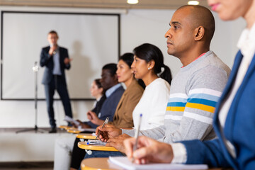 Concentrated Hispanic man sitting in conference room listening to lecturer and making notes during business training