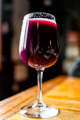 Glass of dark red purple black grape juice as wine on wooden table closeup of one drink and bokeh background vertical view