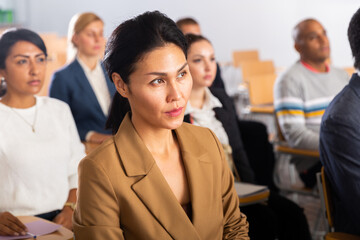 Portrait of young focused woman sitting and listening to speaker at business conference