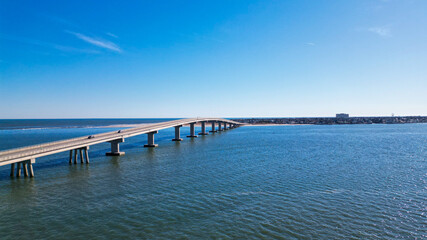 Aerial drone view of a smooth long bridge over a dark blue body of water