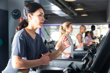 Fototapeta na wymiar Athletic girls running on treadmill in fitness club