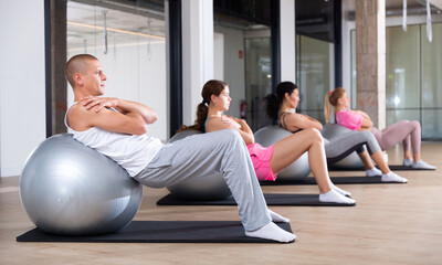 Focused young adult man doing workout with fitness ball during group pilates training