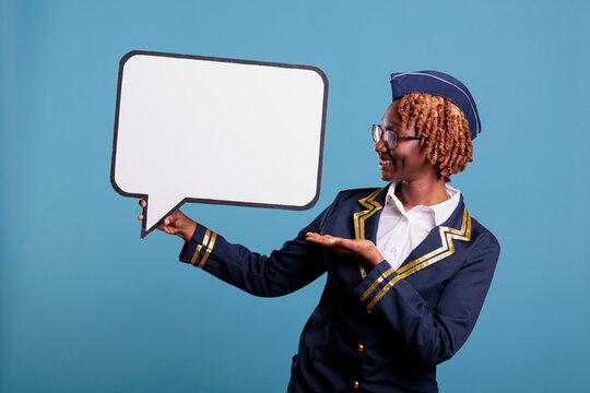 African American Female Flight Attendant Holding Speech Balloon. Smiling Air Hostess Studio Portrait With Banner Next Her. Uniformed Stewardess Holding Dialogue Window.