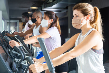 Active people in protective masks having running elliptical trainer class in health club