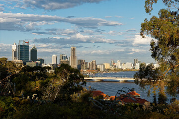Obraz premium View to the centre of Perth in Western Australia, landscape with the skyscrapers, parks and bay with the bridge during sunset or sunrise. Clouds on the dramatic blue sky