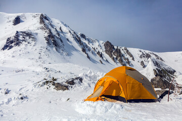 Hikers set orange tent in winter mountains. Alpinism sport