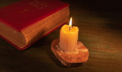 Close up of a closed bible and a lit candle on a wooden background
