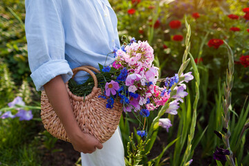 Close up of straw bag filled with flowers. Woman holding summer purse with bouquet of blooms....