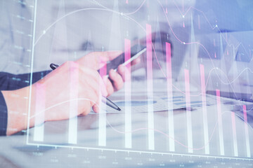 Double exposure of man's hands holding and using a phone and financial chart drawing. Market analysis concept.