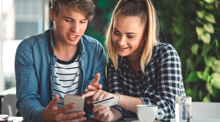 Cheerful caucasian young couple online shopping on the phone, woman holding a credit card in her hands