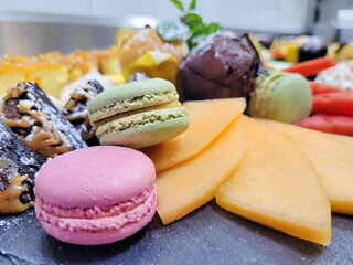 beautiful and tasty dessert plate consisting of multi-colored macarons, chocolate brownie, fruits and berries - melon and watermelon - for a good rest, party, romantic meeting, weekend