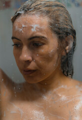 Fototapeta na wymiar artistic photo of sensual woman in a soapy bath with foam behind the glass door taking a bath in the shower