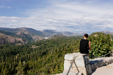 Mountain summer landscape on a sunny day. A young guy sits on the rocks and admires the picturesque view of the mountains, the beautiful blue sky with clouds. Young man resting in the mountains
