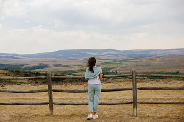 A young brown-haired girl looks into a mountain landscape. Spring panorama with mountains and cloudy sky. Elk Mountain, Wyoming, USA