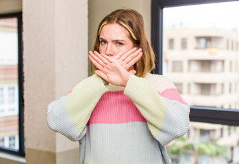 pretty caucasian woman covering face with hand and putting other hand up front to stop camera,...
