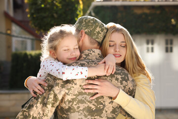 Daughter and wife hugging soldier in Ukrainian military uniform outdoors. Family reunion