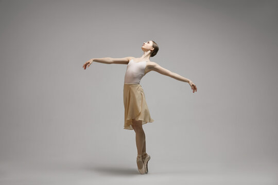 Young ballerina practicing dance moves on grey background. Space for text