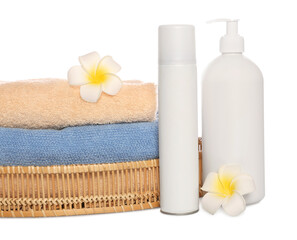 Obraz na płótnie Canvas Soft towels in wicker basket, bottles of cosmetic products and plumeria flowers on white background
