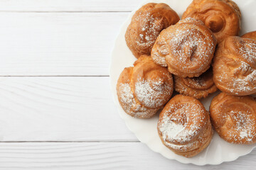 Delicious profiteroles with powdered sugar on white wooden table, top view. Space for text