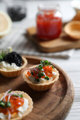 Delicious tartlets with red and black caviar served on white wooden table, closeup. Space for text