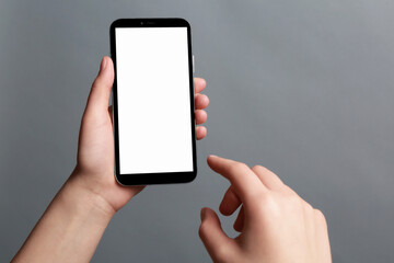 Woman holding smartphone with blank screen on grey background, closeup. Mockup for design
