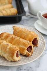 Delicious sausage rolls and hot drink on white marble table, closeup