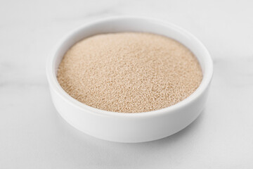 Bowl of active dry yeast on white marble table, closeup