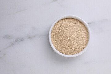 Bowl of active dry yeast on white marble table, top view. Space for text