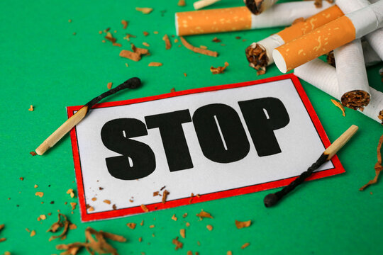 Stop smoking concept. Card with word Stop, cigarette stubs, tobacco and burnt matches on green background, closeup