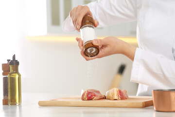 Professional chef adding pepper to delicious meat at white marble table, closeup