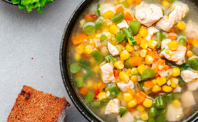 Hot vegetable soup with chicken, corn and green beans. Comfort food. Gray table background, top view