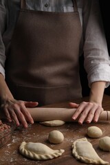 Fototapeta premium Woman rolling dough for chebureki on wooden table, closeup
